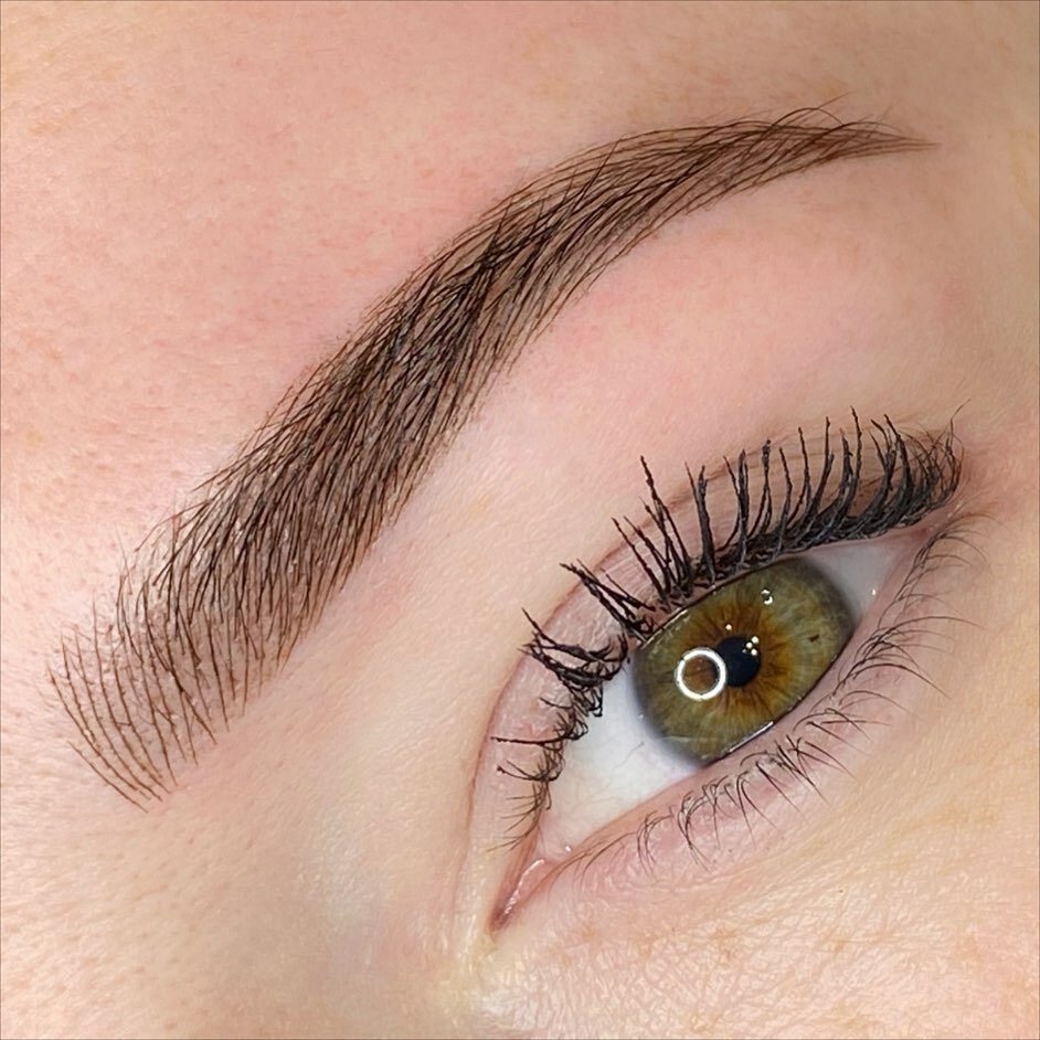Macro detail of feathered cosmetic tattoo brows above a green eye